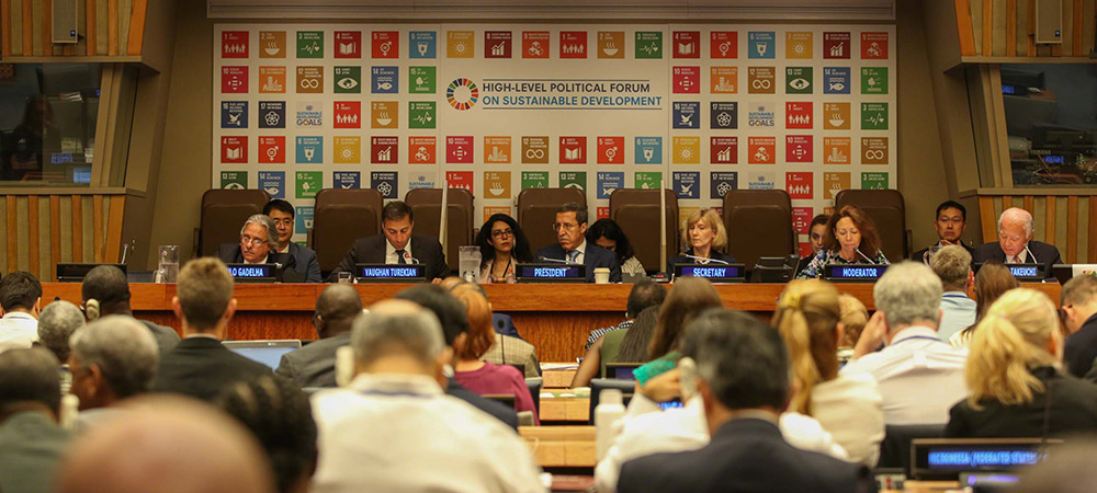 Delegates sitting at the plenary podium sitting infront of the HLPF banner.