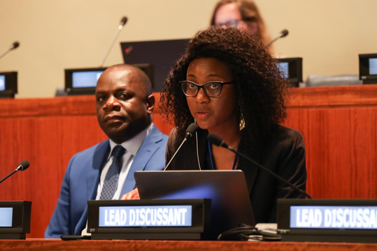 A woman delivering an intervention, a man sitting behind her looking into the camera.